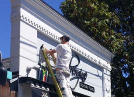 painter working on ladder outside Aubergine's storefront in Victoria